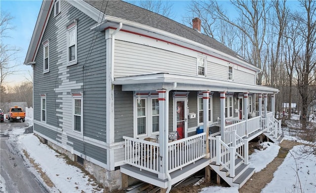 view of front of property featuring covered porch, a chimney, and roof with shingles