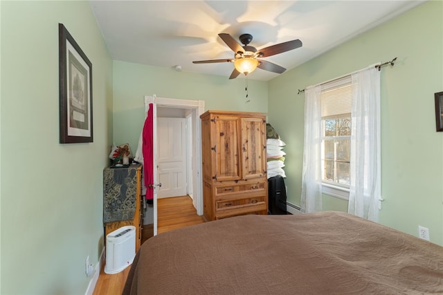 bedroom with light wood-type flooring, ceiling fan, and baseboard heating