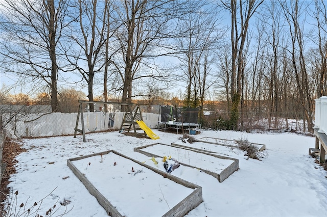 snowy yard with a trampoline, a playground, and fence