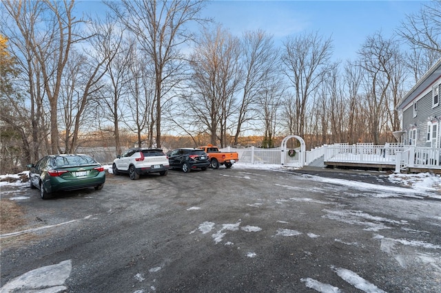 snow covered parking area with a gate, uncovered parking, and fence