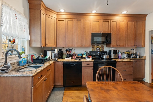 kitchen with light stone counters, light wood finished floors, recessed lighting, a sink, and black appliances