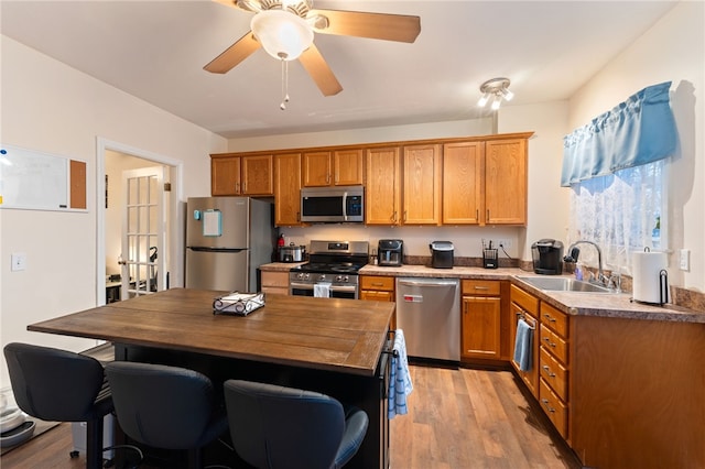 kitchen featuring brown cabinets, appliances with stainless steel finishes, a ceiling fan, a sink, and light wood-type flooring