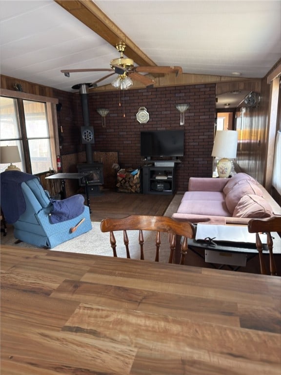 living area featuring vaulted ceiling with beams, wooden walls, wood finished floors, a ceiling fan, and a wood stove