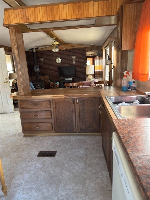 kitchen featuring lofted ceiling with beams, a sink, visible vents, dishwasher, and a wood stove