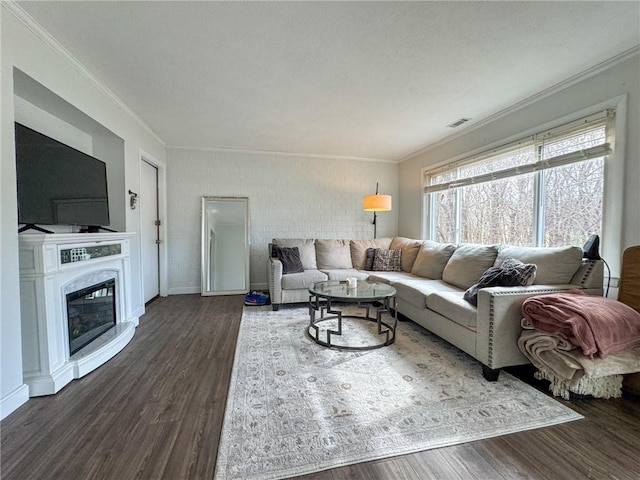 living room featuring dark wood-style floors, visible vents, ornamental molding, and a glass covered fireplace