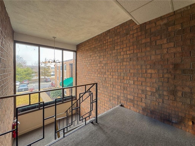 interior space with carpet floors, a notable chandelier, a textured ceiling, an upstairs landing, and brick wall