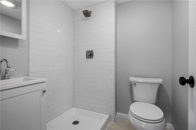 bathroom with tile patterned flooring, toilet, vanity, baseboards, and a tile shower