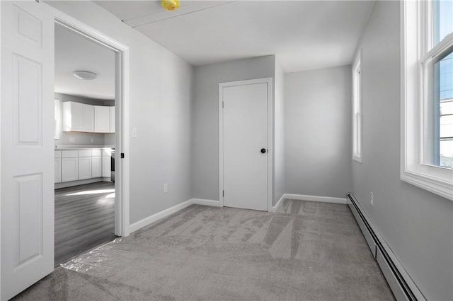 spare room with a baseboard radiator, light colored carpet, and baseboards