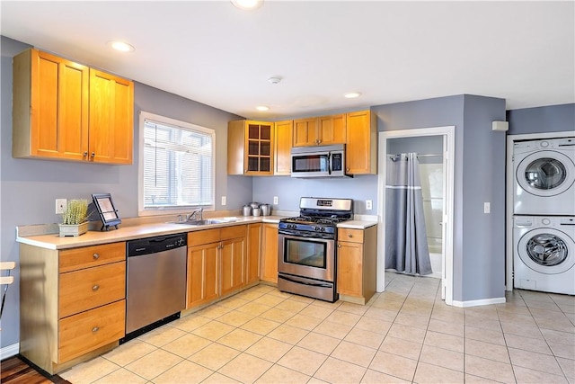 kitchen featuring stacked washer and clothes dryer, light tile patterned floors, light countertops, appliances with stainless steel finishes, and a sink