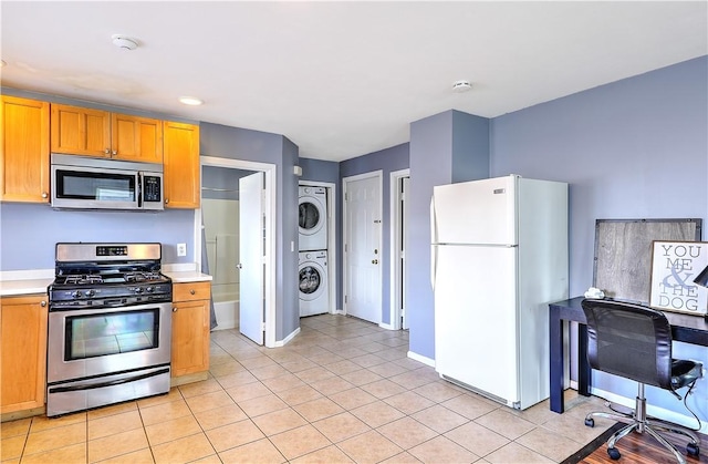 kitchen featuring light tile patterned flooring, stainless steel appliances, baseboards, light countertops, and stacked washing maching and dryer