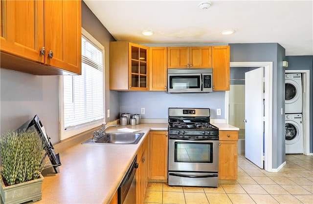 kitchen with light tile patterned floors, stainless steel appliances, stacked washer and dryer, light countertops, and a sink