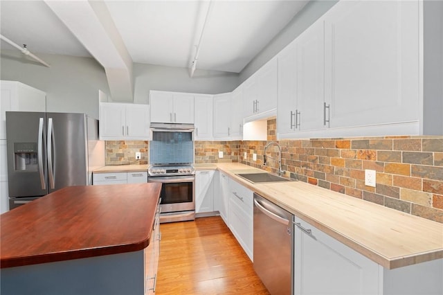 kitchen with tasteful backsplash, butcher block countertops, appliances with stainless steel finishes, under cabinet range hood, and a sink