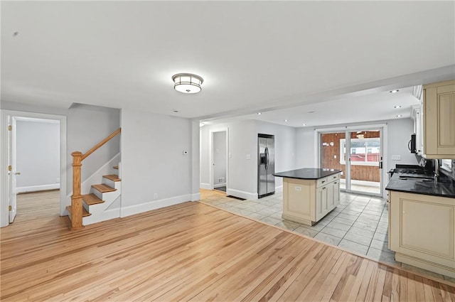 kitchen with a center island, cream cabinetry, stainless steel refrigerator with ice dispenser, light wood finished floors, and dark countertops