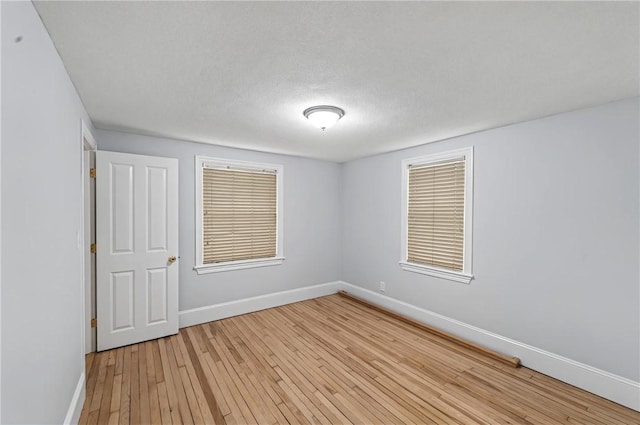 spare room featuring a textured ceiling, light wood-type flooring, and baseboards