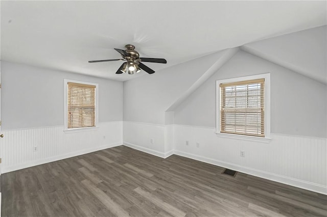 bonus room featuring dark wood-style floors, visible vents, a ceiling fan, and wainscoting