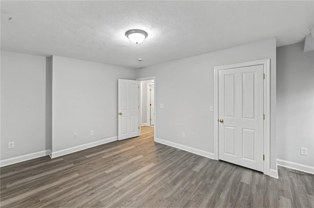 unfurnished bedroom featuring a textured ceiling, baseboards, and wood finished floors