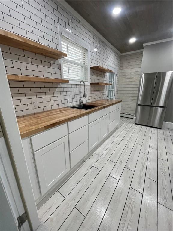 kitchen featuring freestanding refrigerator, a sink, light wood-type flooring, open shelves, and wooden counters