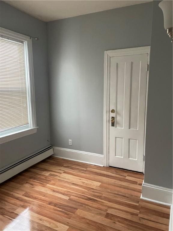 unfurnished room with a baseboard radiator, light wood-style flooring, and baseboards