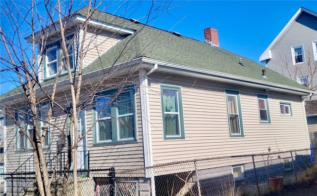 view of side of property featuring a fenced front yard, a chimney, and roof with shingles