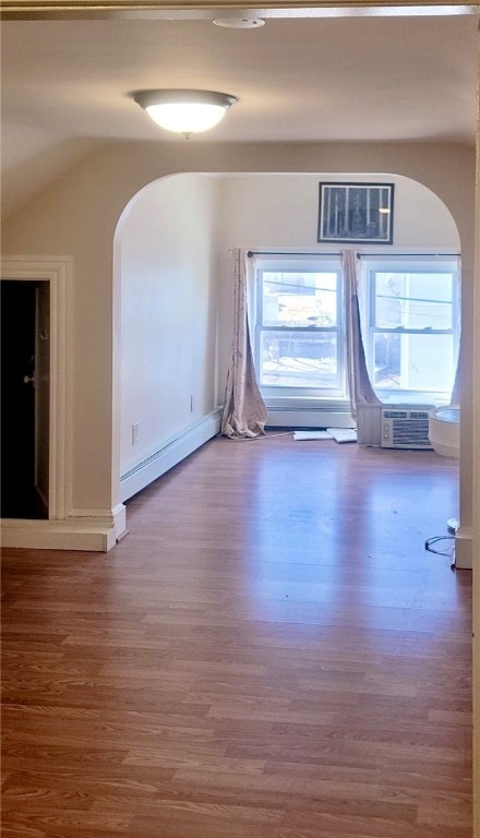 empty room with a baseboard radiator, cooling unit, arched walkways, and wood finished floors