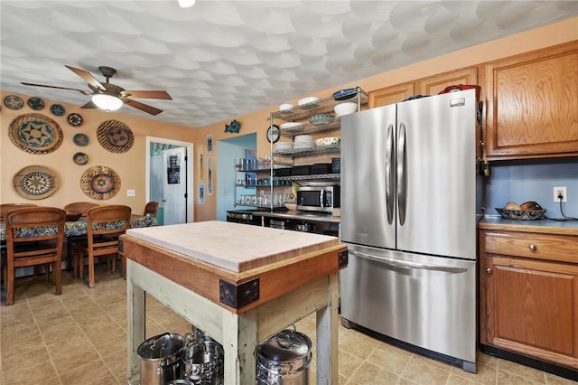 kitchen with butcher block countertops, appliances with stainless steel finishes, ceiling fan, and a center island