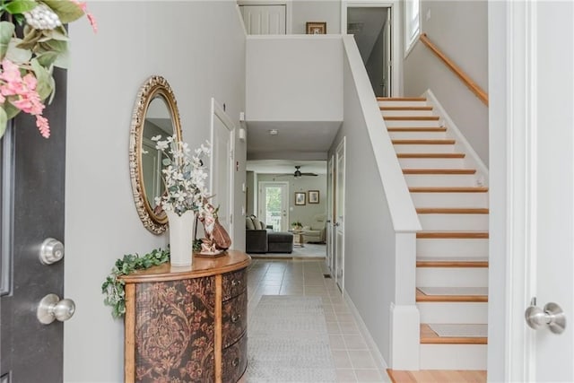 foyer entrance with tile patterned floors, baseboards, a ceiling fan, and stairs