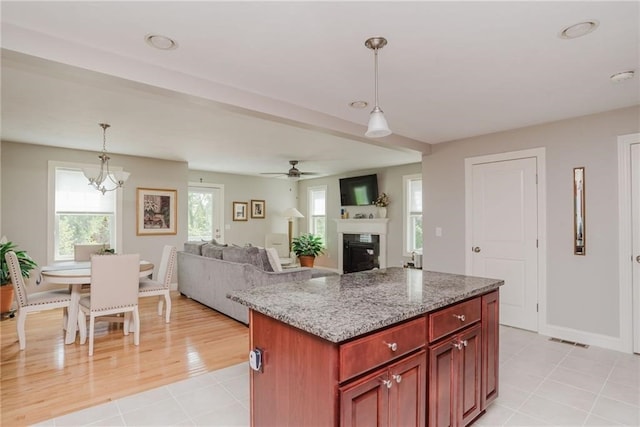 kitchen featuring visible vents, decorative light fixtures, reddish brown cabinets, a fireplace, and light stone countertops