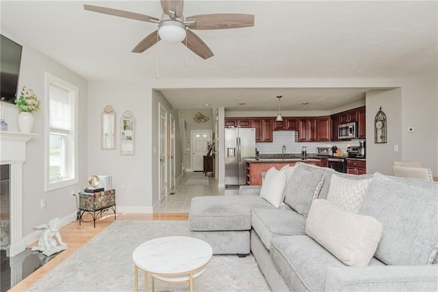 living room featuring a tiled fireplace, a ceiling fan, light wood-type flooring, and baseboards