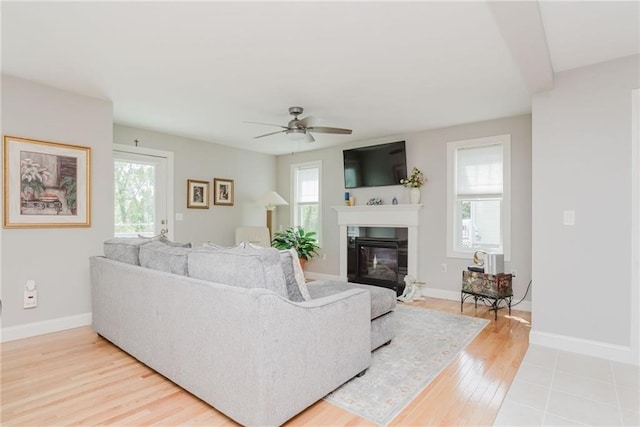 living room with a glass covered fireplace, baseboards, light wood-style floors, and a ceiling fan