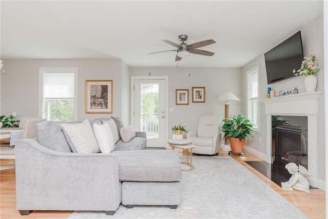 living area with a fireplace with flush hearth, ceiling fan, baseboards, and wood finished floors