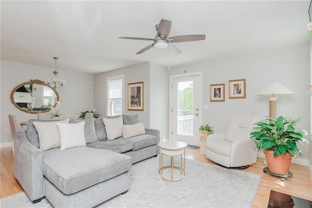 living room featuring ceiling fan with notable chandelier, baseboards, and wood finished floors