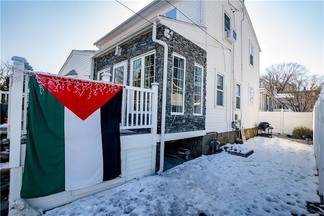 view of snowy exterior with fence and stone siding