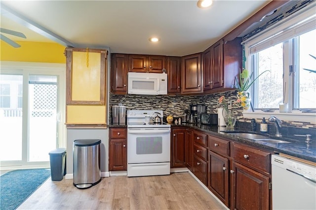 kitchen with light wood-style flooring, a sink, dark stone countertops, backsplash, and white appliances