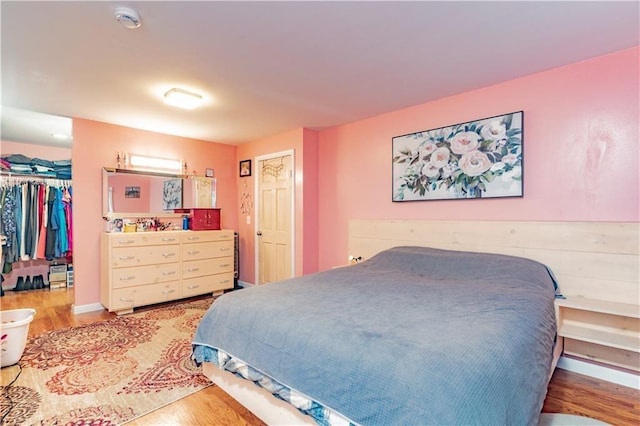 bedroom with a walk in closet and wood finished floors