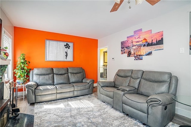 living room with a ceiling fan, an accent wall, baseboards, and wood finished floors