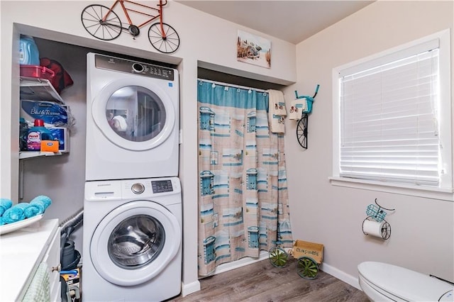 laundry room featuring baseboards, wood finished floors, laundry area, and stacked washing maching and dryer