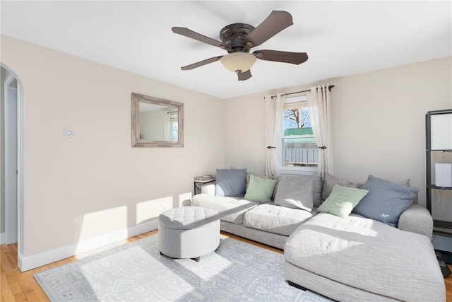 living area with light wood-type flooring, arched walkways, baseboards, and ceiling fan