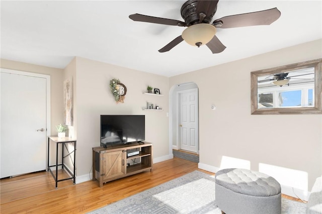 living area with baseboards, arched walkways, and light wood finished floors