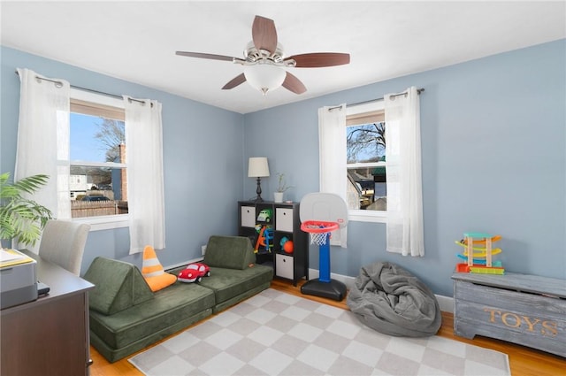 sitting room featuring a wealth of natural light, a ceiling fan, baseboards, and wood finished floors