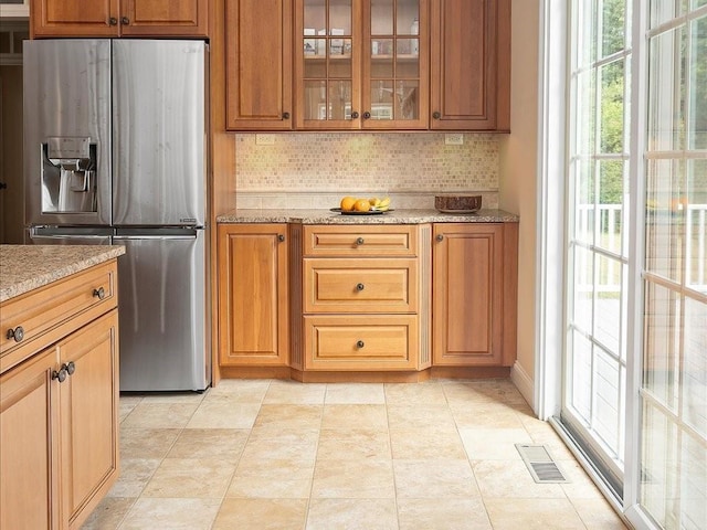 kitchen featuring light stone counters, visible vents, stainless steel fridge, and glass insert cabinets