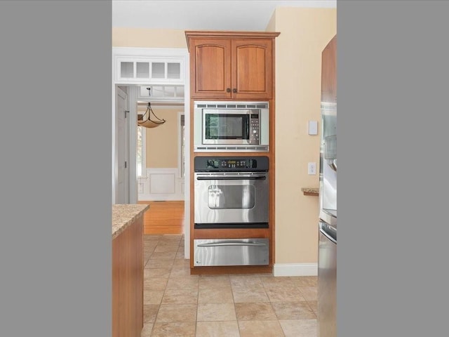 kitchen featuring a warming drawer, light stone counters, brown cabinetry, and stainless steel appliances