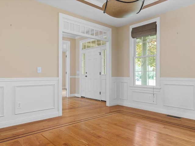 foyer entrance with light wood finished floors, visible vents, and a wainscoted wall