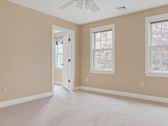 spare room featuring light carpet, visible vents, ceiling fan, and baseboards