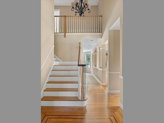 staircase with baseboards, a notable chandelier, and a towering ceiling