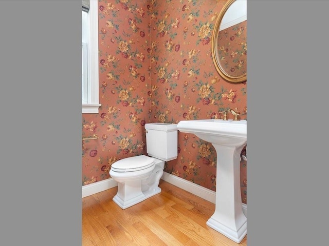 bathroom with toilet, wallpapered walls, baseboards, and wood finished floors