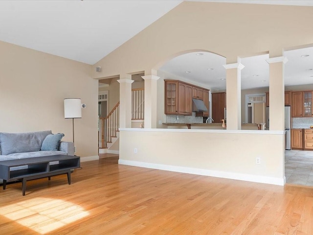 living area featuring stairway, light wood finished floors, baseboards, and ornate columns