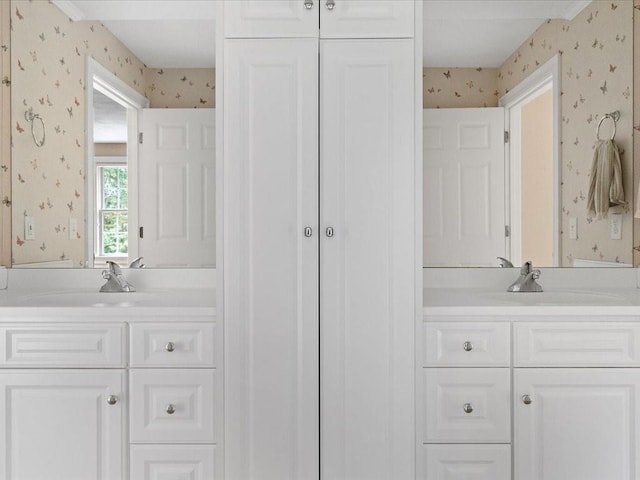 full bath featuring a sink, two vanities, and wallpapered walls