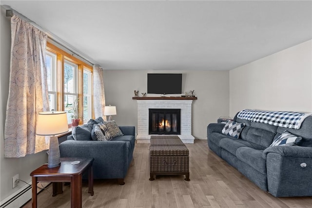 living room with a fireplace, a baseboard heating unit, and light wood-style floors