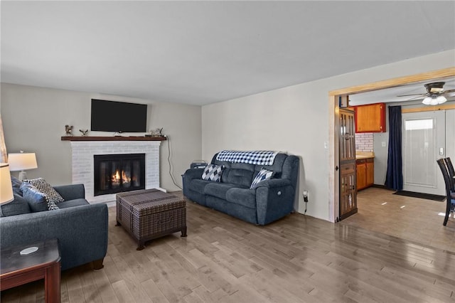 living area with a ceiling fan, light wood-style flooring, and a fireplace