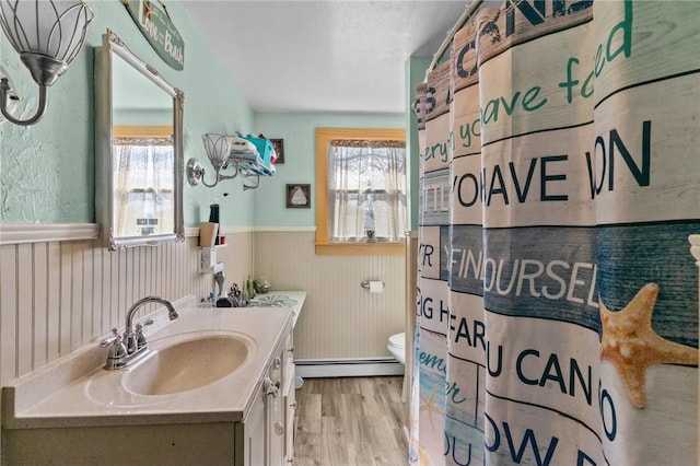 full bath featuring vanity, wood finished floors, a healthy amount of sunlight, and a wainscoted wall